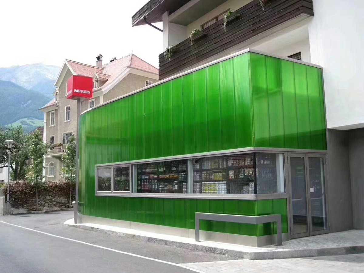 Green interlocking polycarbonate panels installed on curved commercial building facade with modern architectural design