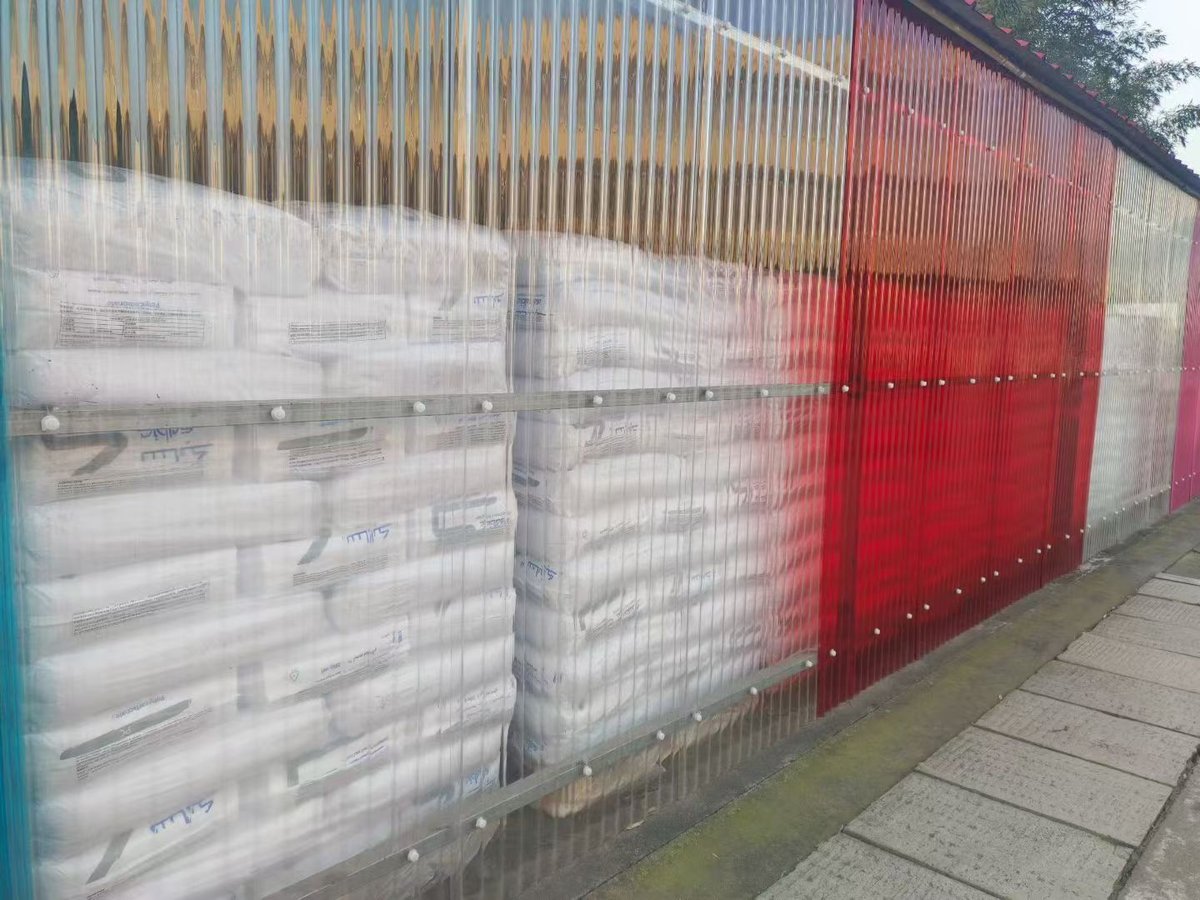 Corrugated polycarbonate protective enclosure — red and translucent panels mounted on metal framework serving as a weather barrier for stored industrial materials