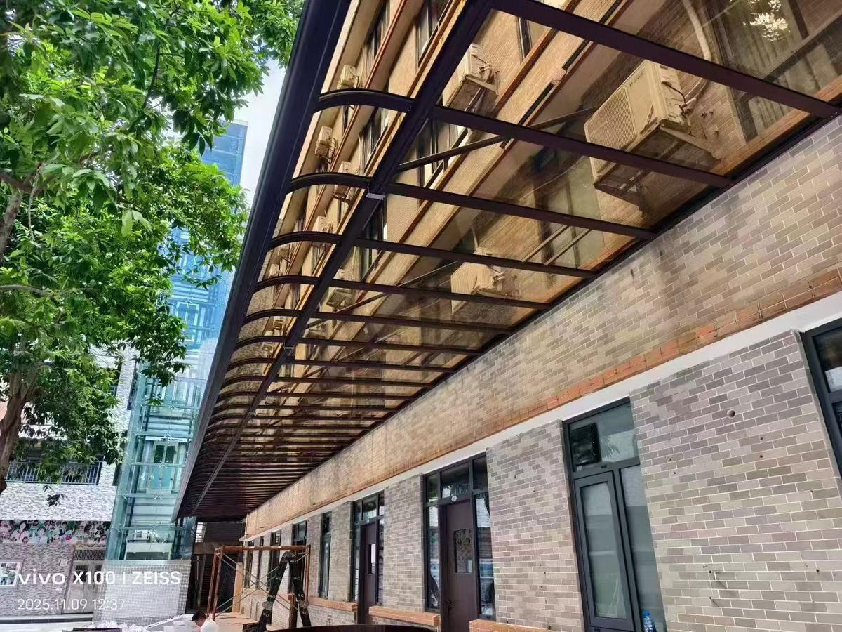 Modern commercial building entrance with solid polycarbonate canopy supported by dark metal framework, showing transparent glazing and urban setting