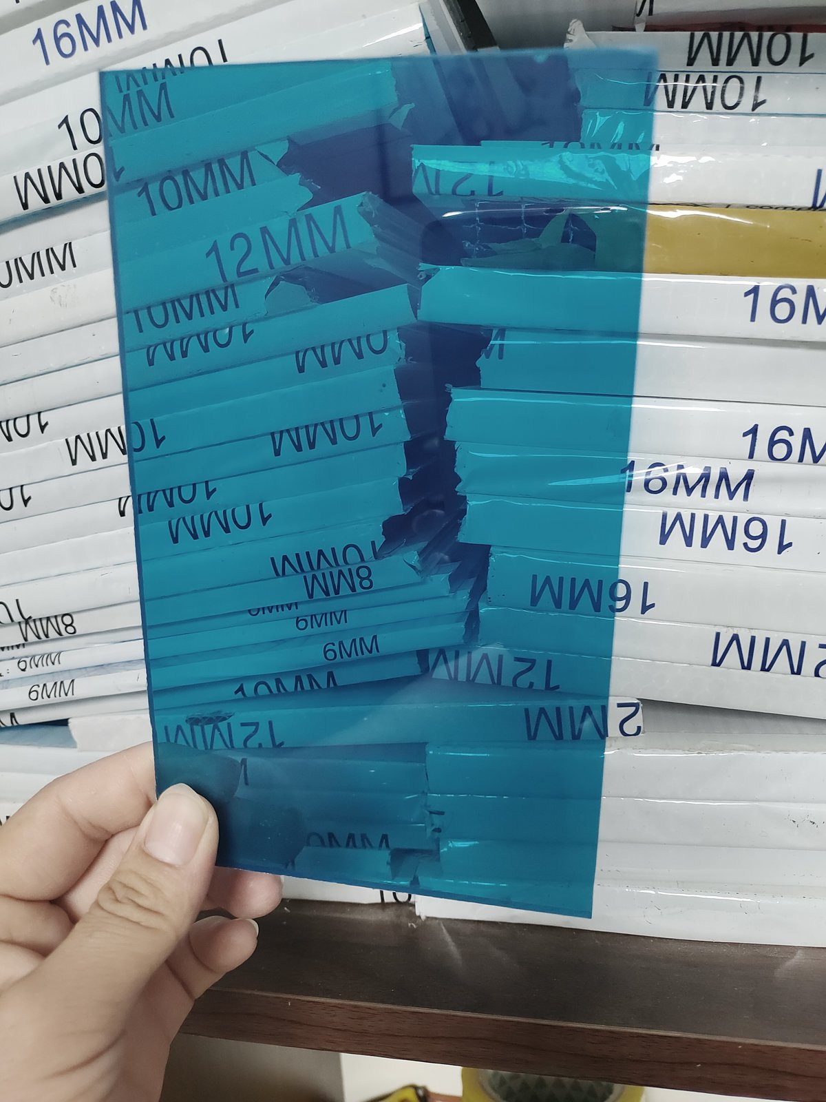 Stack of blue translucent solid polycarbonate sheets with thickness labels from 6mm to 16mm, showing available color and thickness range