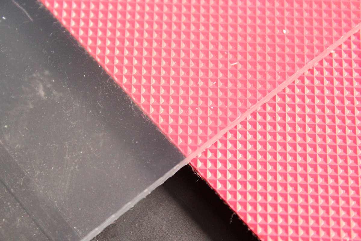 Clear transparent solid polycarbonate sheet next to red textured diamond-pattern PC sheet, illustrating the range of colours and surface finishes available