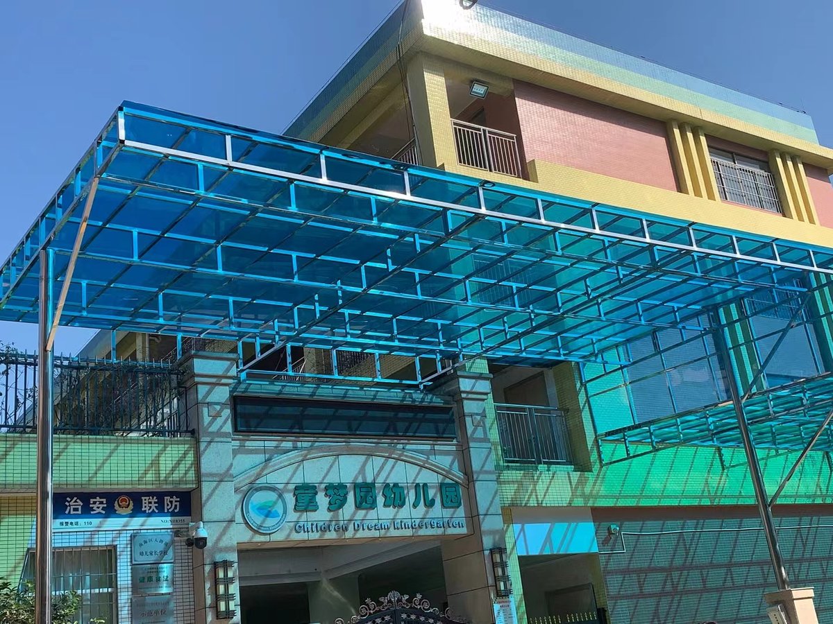Wide-angle view of blue solid polycarbonate sheet canopy on grid framework at kindergarten, showing structural installation and light diffusion
