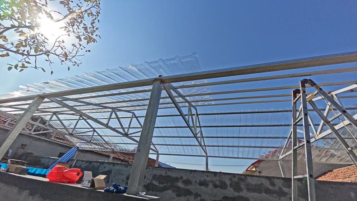 Worker installing corrugated polycarbonate sheets on a carport steel frame