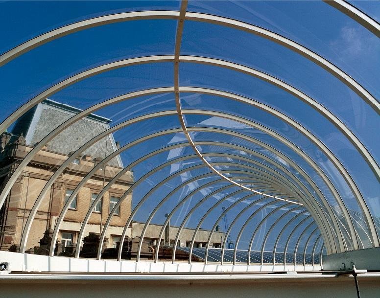 Curved solid polycarbonate walkway canopy cold-bent over an aluminium arch