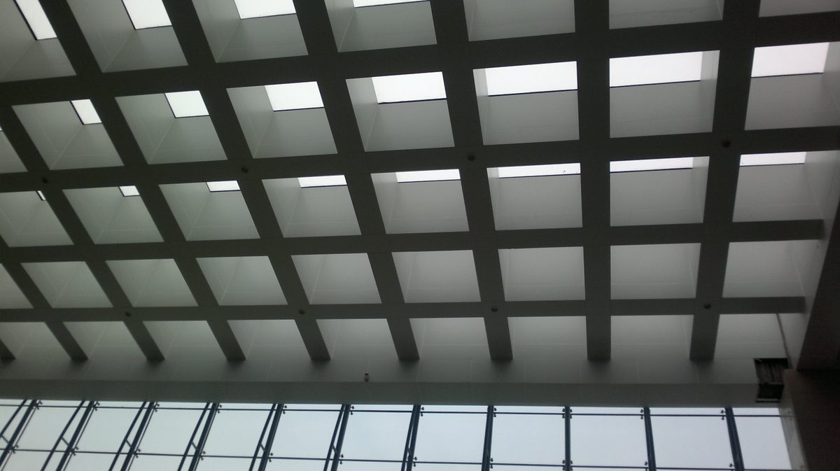 Interior of a hospital atrium with a grid of translucent polycarbonate skylight panels diffusing daylight over the hall below