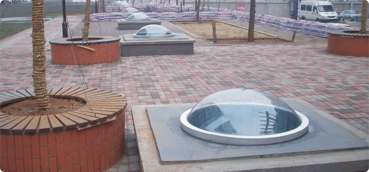 Round polycarbonate dome skylight set into a paved public plaza, lighting the underground space below